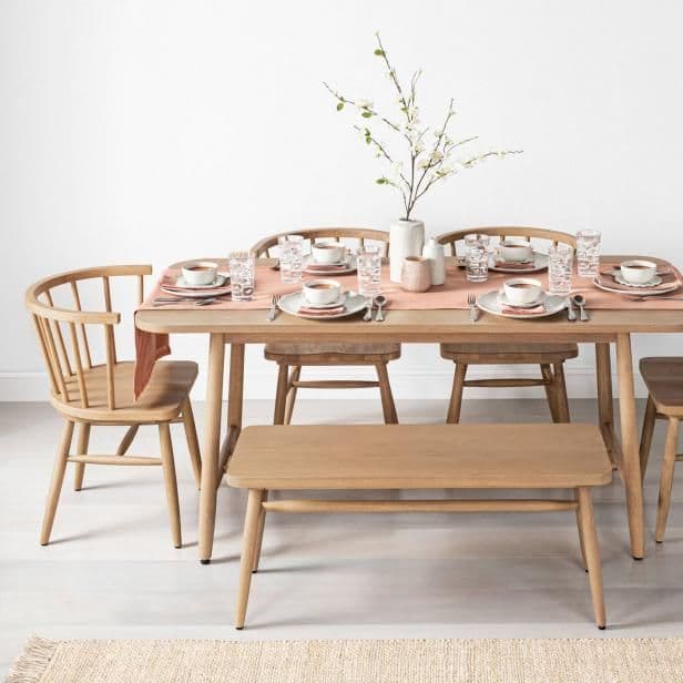 A simple wooden dining table adorned with pink and green decor accents, all of which come from Chip and Joanna Gaines' new Target furniture collection.