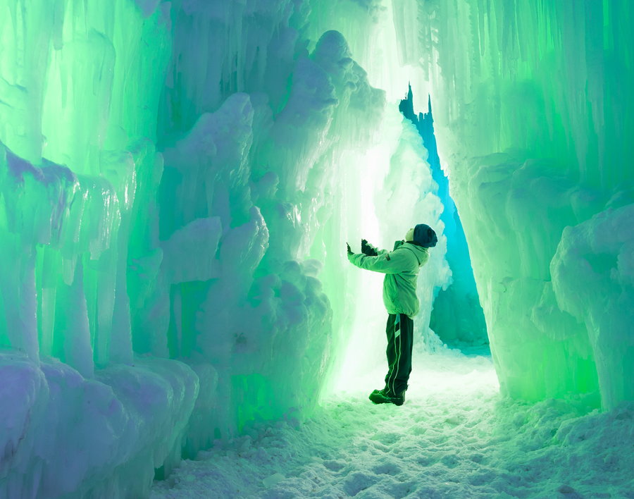 Child strokes a glowing green wall of ice inside one of Brent Christensen's Ice Castles.