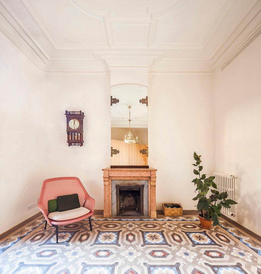 The living area inside the small Barcelona apartment boasts simple walls, pastel furniture pieces, and a bold historic floor. 