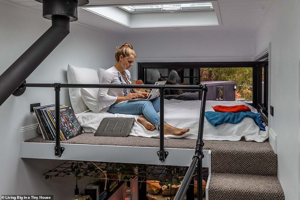 Lisa Tranter checks her computer on a cozy lofted guest bed inside her ultramodern DIY tiny home. 