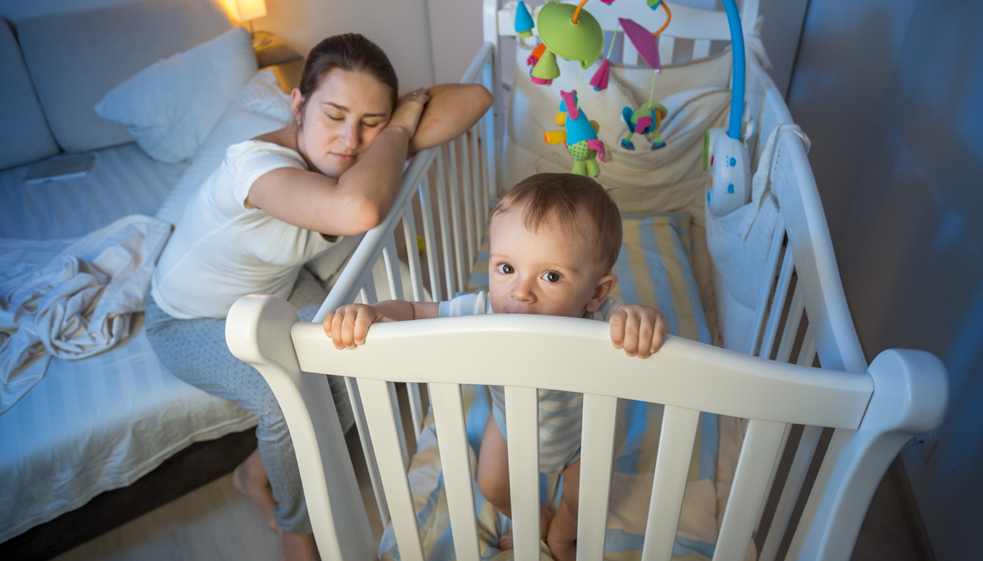 tired mom of toddler resting head on crib