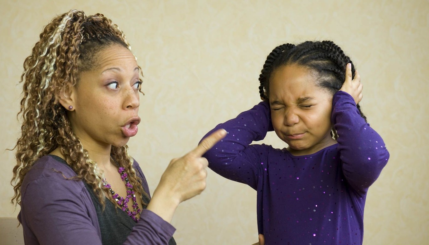 child covers her ears as mother scolds her