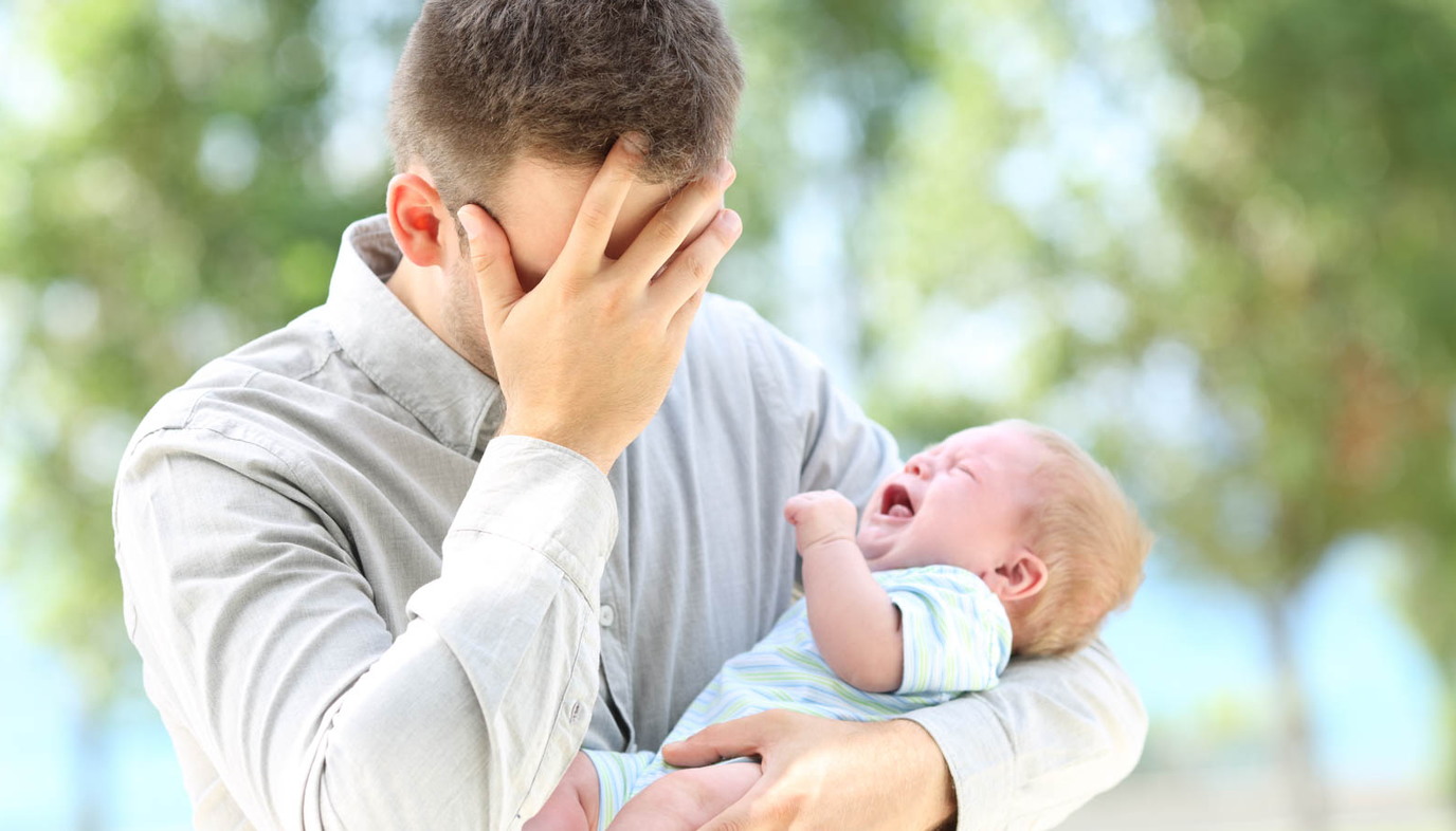 Father with face in hand holding crying baby