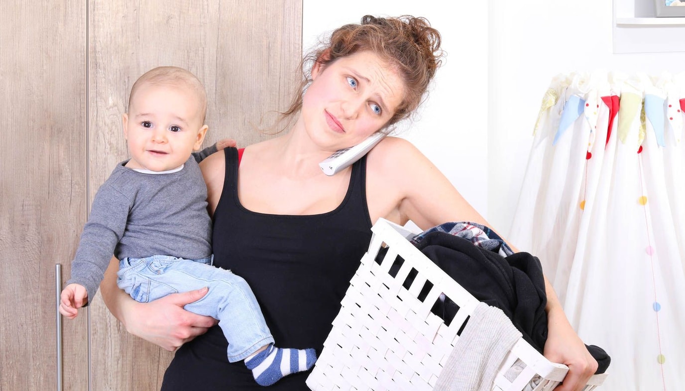 parent with child new mom exhaustion on phone doing laundry