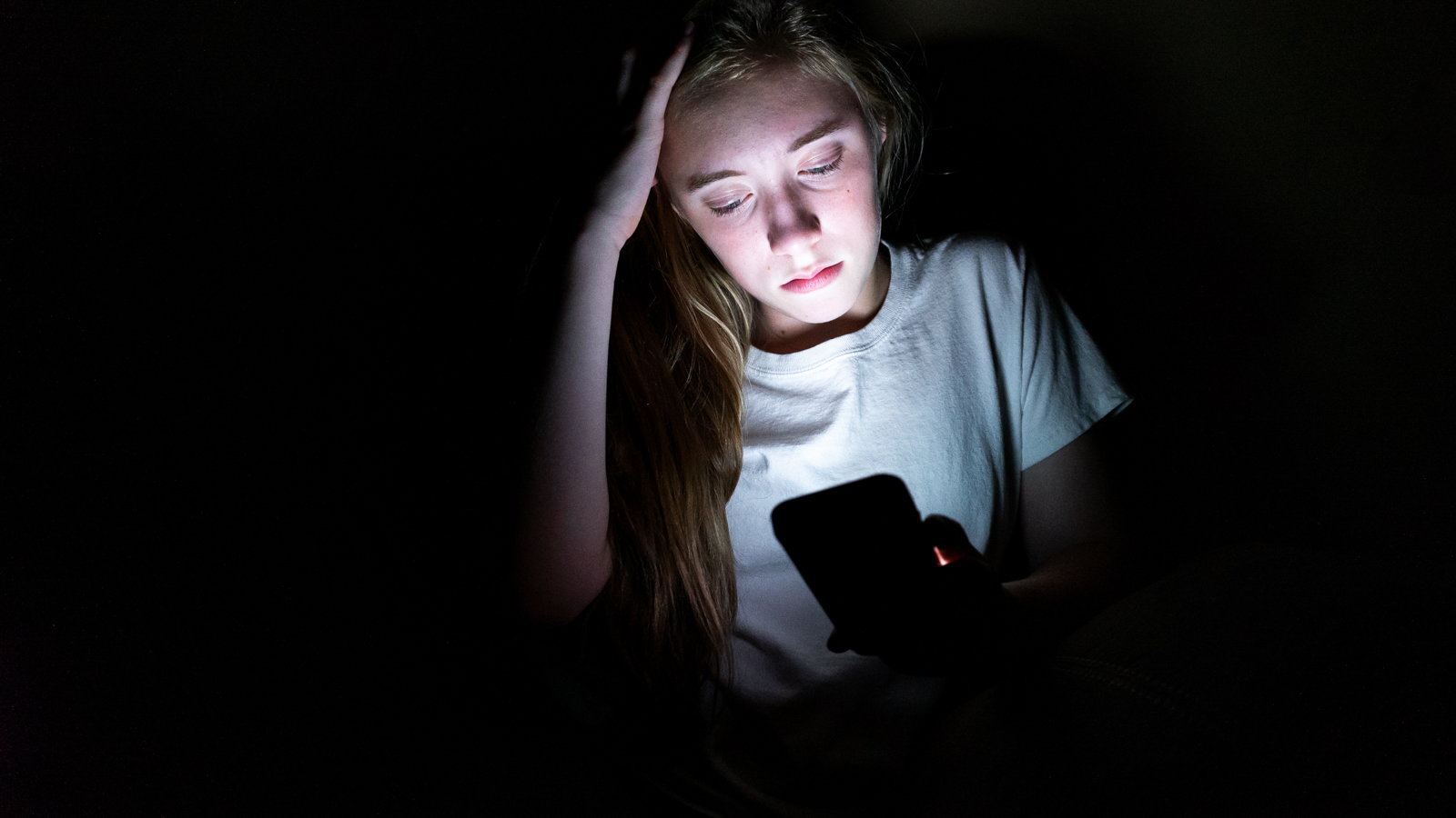 sad teen in dark room looking at smartphone