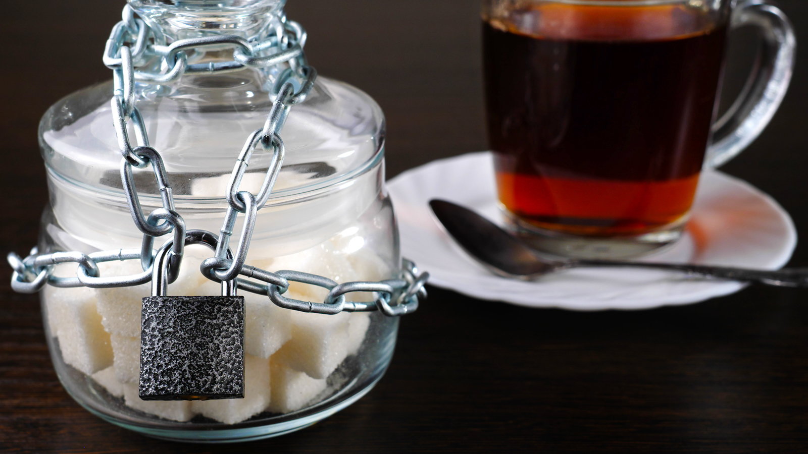 jar of sugar locked with padlock next to tea cup