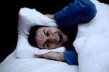 man covering ears with pillow