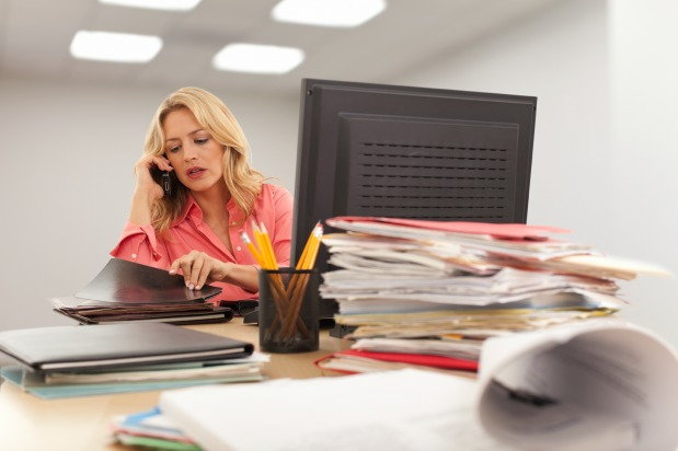 woman talking on the phone while looking at paperwork in front of desktop computer
