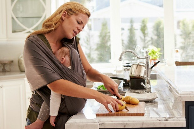 Mother carries child on sling while preparing dinner and talking on the phone