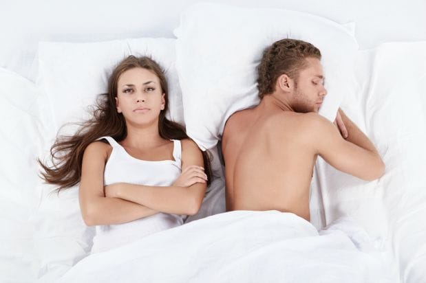 couple laying in bed featuring man sleeping soundly and woman awake and angry