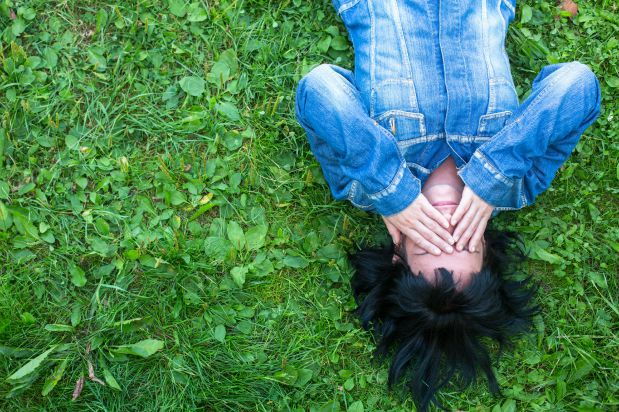Woman laying on grass while covering her eyes with her hands