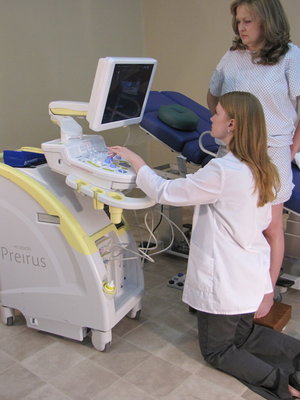 Demonstrates the current practice of scanning for reflux with patient standing and sonographer kneeling using awkward postures and excessive reaching.