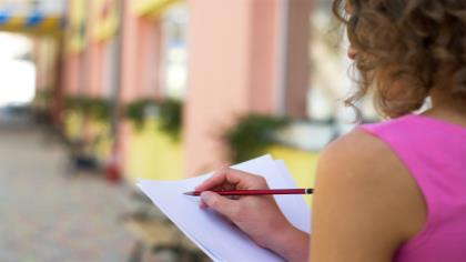 A woman sits outside preparing to write with pencil and paper.