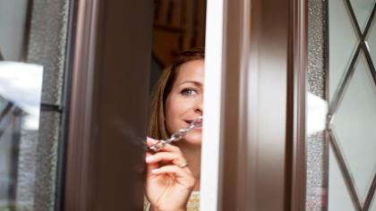 A woman peeks around the front door to see who's there. 