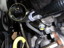The best way to get to the block heater screw plug is from a 45 degree side angle instead of straight down past the valve cover and ignition sticks that are in the way.

Unplug the connector that goes to the front O2 sensor by depressing the tab on it and pulling up on it. (yellow circle)

Unplug the O2 sensor connector from the metal bracket by depressing the tab on it and pushing it downwards.

Unbolt the bolt holding the bracket (yellow dot) using a 14 mm socket.

Lift the automatic transmiss