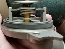 It comes already fitted into the aluminum housing.  Yo see here the two "wings" on the thermostat which slot into these grooves on the housing.  It's a secure pressure-fit between here and the second round stamping on the thermostat which seats into the housing...