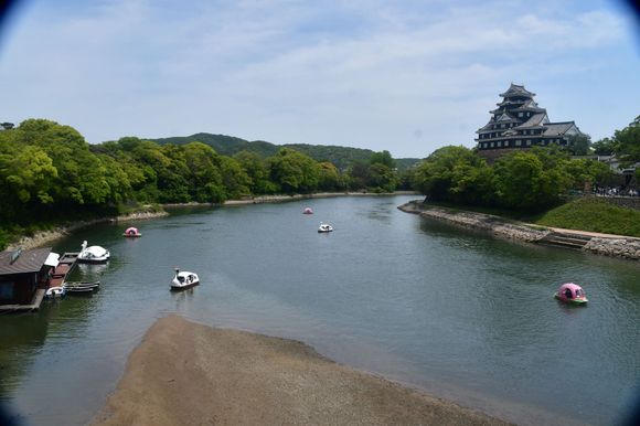 The castle from the footbride across the Asahi  river. Boats for rent just outside the garden including peach shaped boats. 