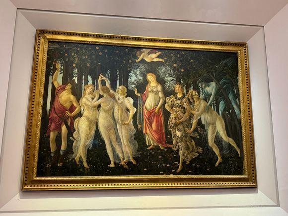 "La Primavera" by Botticelli. The scene takes place in Venus' garden. The goddess is in the center of the painting, and Cupid flies above her, his arrow aimed at one of the three Graces.