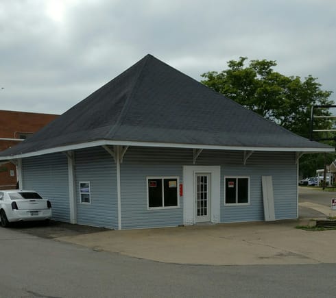 This small building started live as the largest, non-terminal, station for the "Harmony Line". The Harmony Line was a short railroad that operated between 1908 and 1931.  This building was the station where the rail line separated into two branches. Sometime after the railroad closed, it became an Amoco gas station. It functioned as a service station for about 50 years. After the station closed, the building was converted to an apartment/rental, which is what it still functions as today.