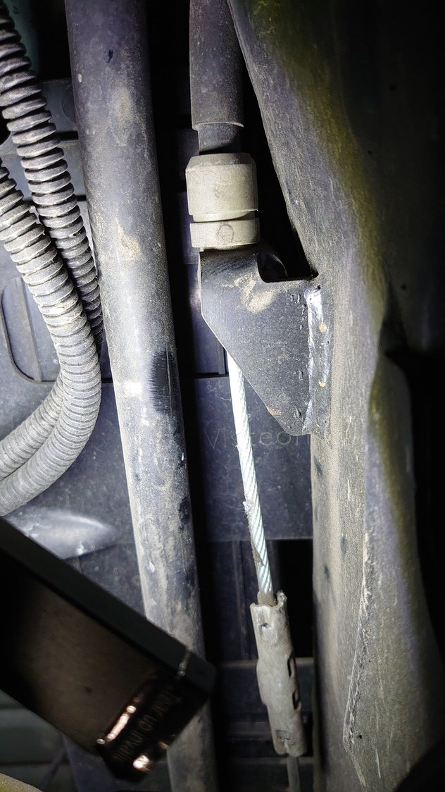 View from the front of the car showing other end of RH parkbrake sheath and its cable still attached to  the central retaining bracket.